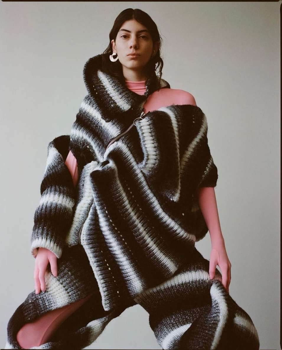 Woman in a cocoon-like striped black and white knitwear garment. She is posing in a neutral indoor setting with soft, diffused lighting.