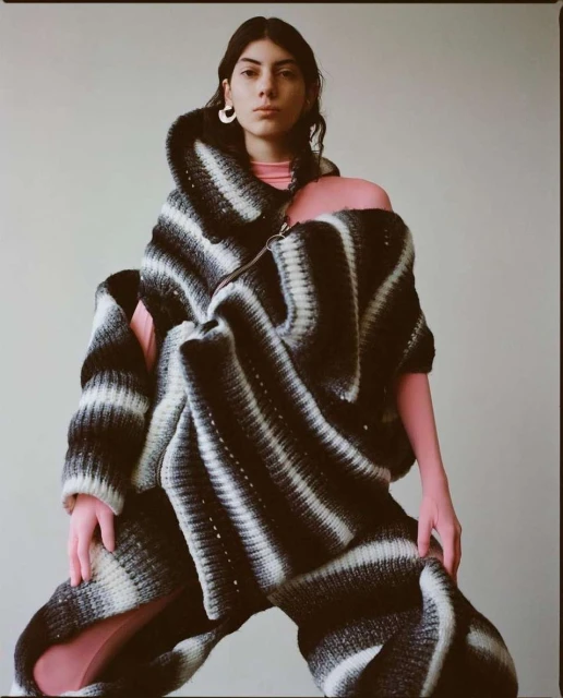 Woman in a cocoon-like striped black and white knitwear garment. She is posing in a neutral indoor setting with soft, diffused lighting.