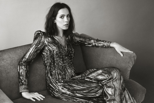 Monochrome portrait of a woman in a metallic dress reclining on a couch, looking directly at the camera with a neutral expression.