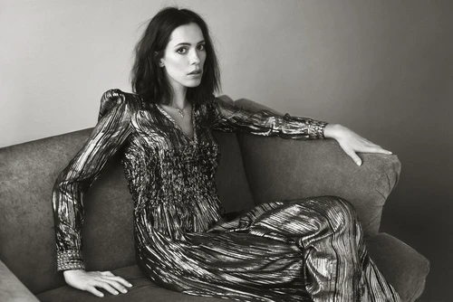 Monochrome portrait of a woman in a metallic dress reclining on a couch, looking directly at the camera with a neutral expression.