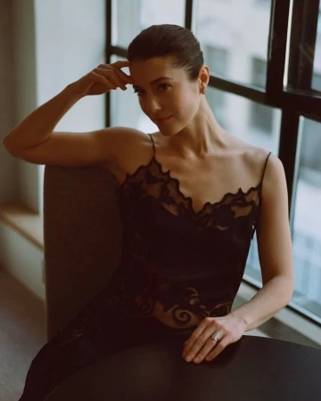 A woman in a black lace camisole seated indoors near a large window by photographer Matthew Priestley.