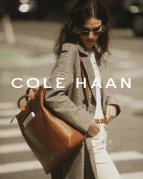 Woman wearing a plaid trench coat and carrying a brown leather backpack on an urban street