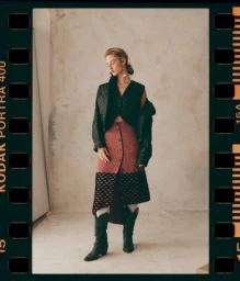 Model wearing a quilted dark jacket, red patterned skirt, and black boots framed inside a 35mm film border.