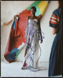 Black female model wearing an avant-garde structured dress with looping purple ribbon embellishments in a studio.