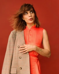 Woman wearing a bright red dress and a plaid blazer draped over her shoulder against a solid red background