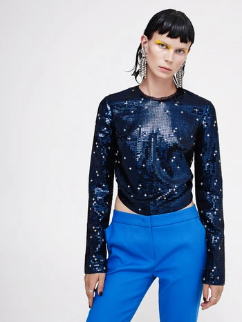 Fashionable adult woman in a sequined top and bright blue pants against a white backdrop, showcasing a modern and stylish clothing ensemble.