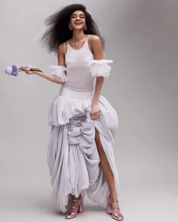 Smiling model in white dress holding a bouquet of flowers against a grey studio seamless background