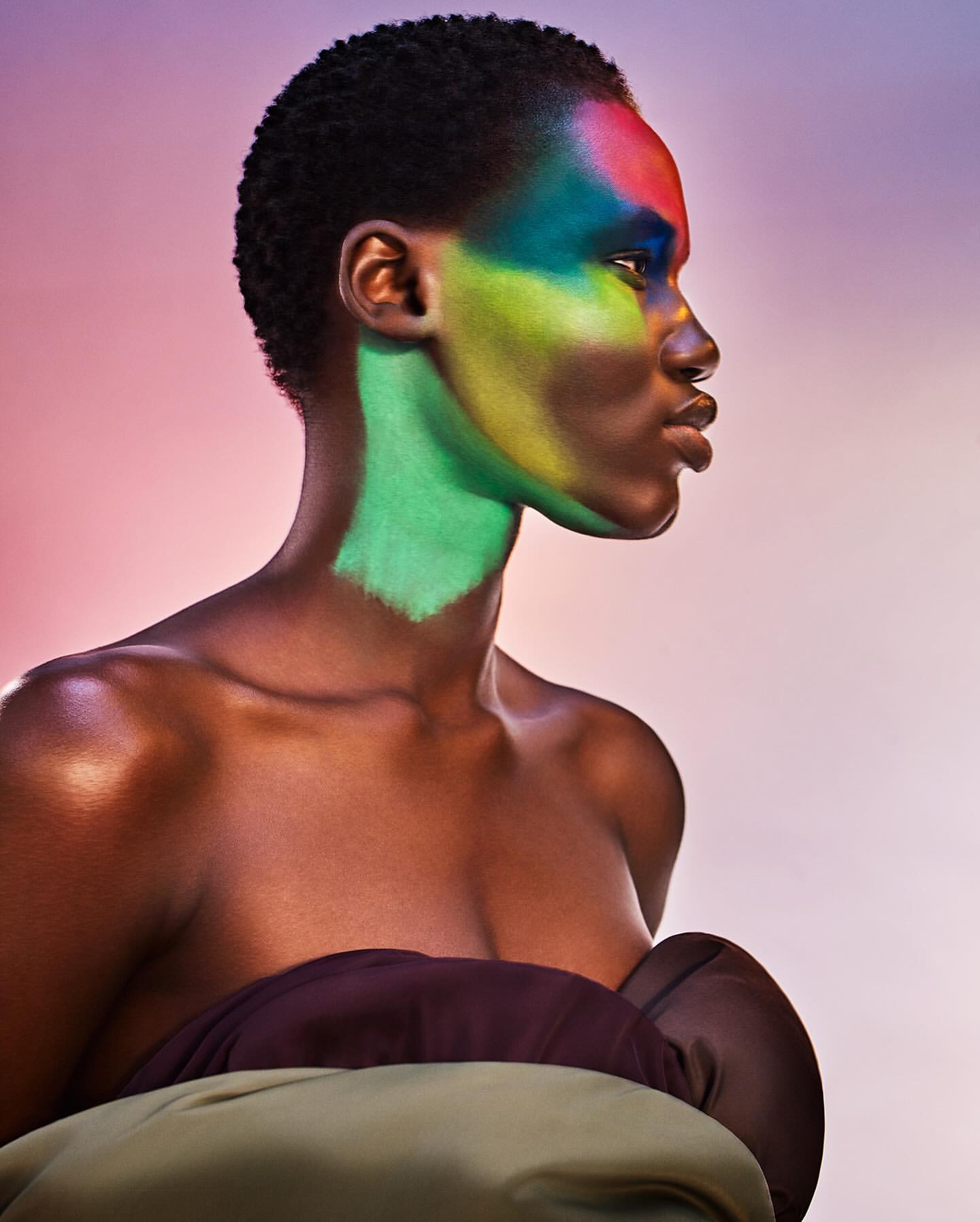 Close-up portrait of a woman with colorful makeup posing against a gradient background in a beauty editorial.