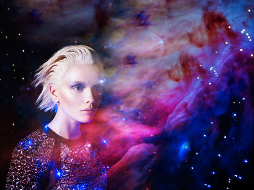 Adult female portrait with short blonde hair and sequin top, set against a vibrant background of purple and blue galaxy nebula.