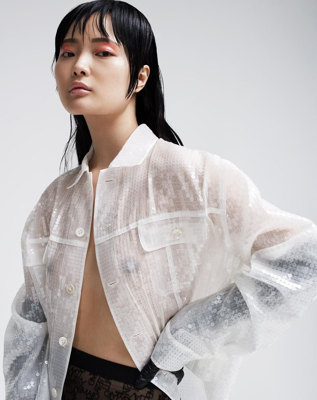 Asian woman in a sequined jacket posing against a light background, showcasing contemporary fashion and beauty trends in a studio setting.