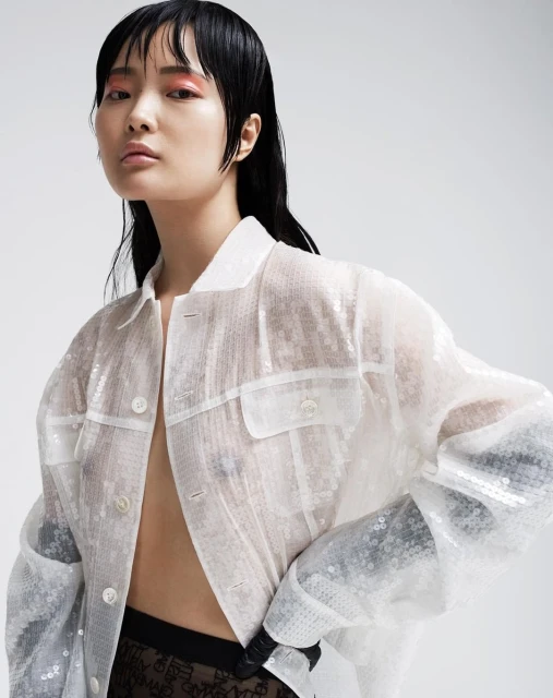 Asian woman in a sequined jacket posing against a light background, showcasing contemporary fashion and beauty trends in a studio setting.