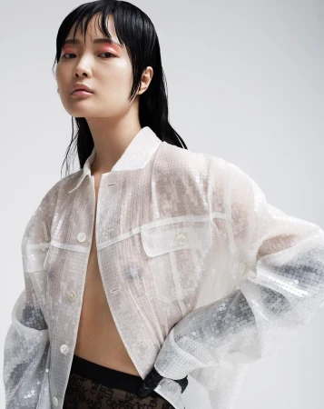 Asian woman in a sequined jacket posing against a light background, showcasing contemporary fashion and beauty trends in a studio setting.