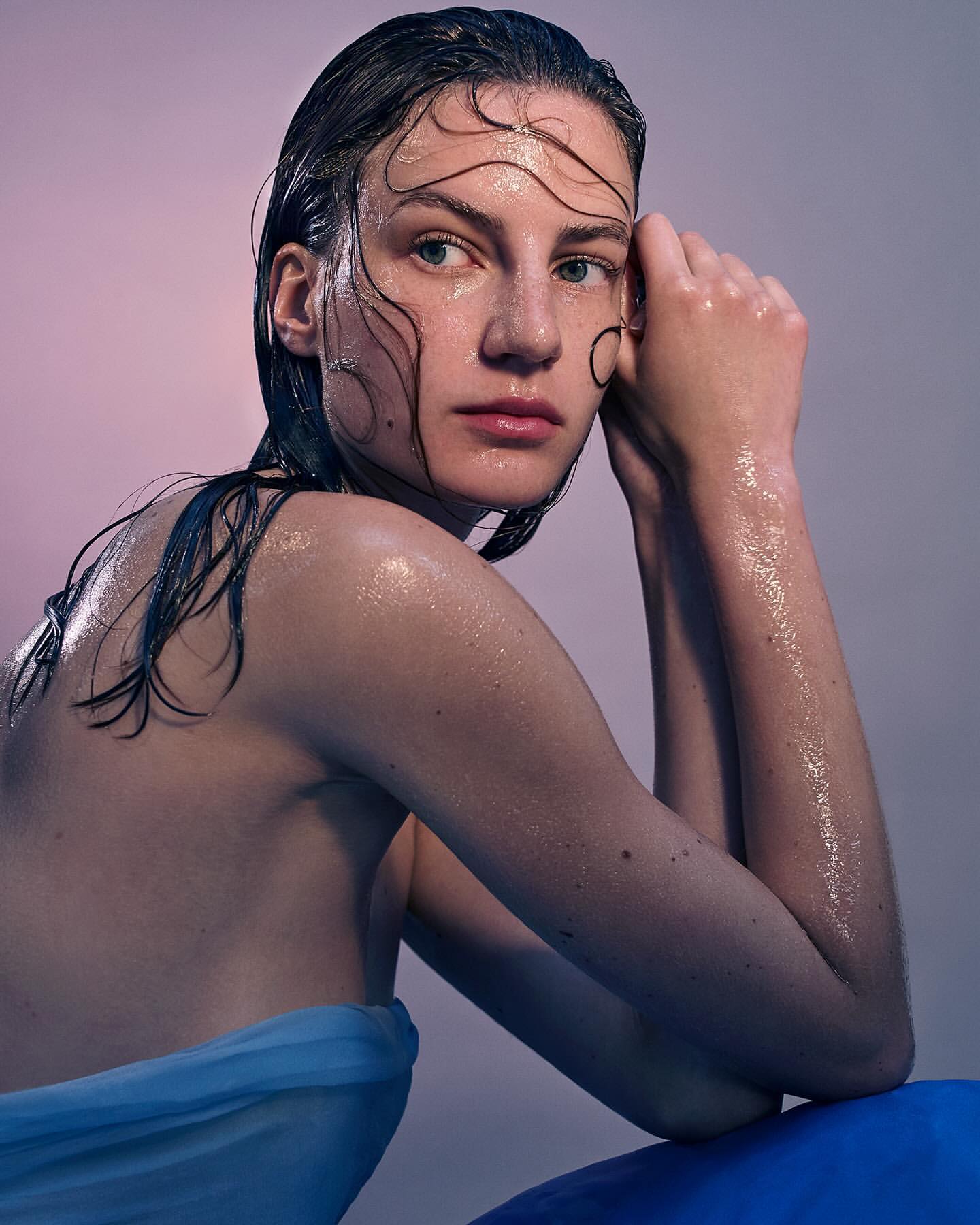 Wet hair fashion shot: An adult female with wet hair and skin poses in a medium studio shot, with a blue draped cloth and sphere.