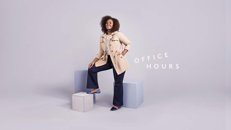 A woman in a trench coat and jeans poses on blocks in a studio with a slight smile, dressed in an outfit for work or a casual outing.