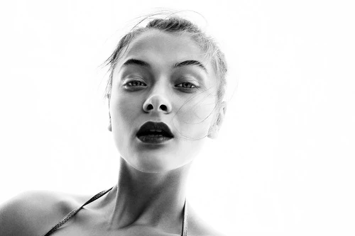Striking black and white portrait of a young adult woman with dark lipstick looking up. Shot from a low angle with bright lighting.