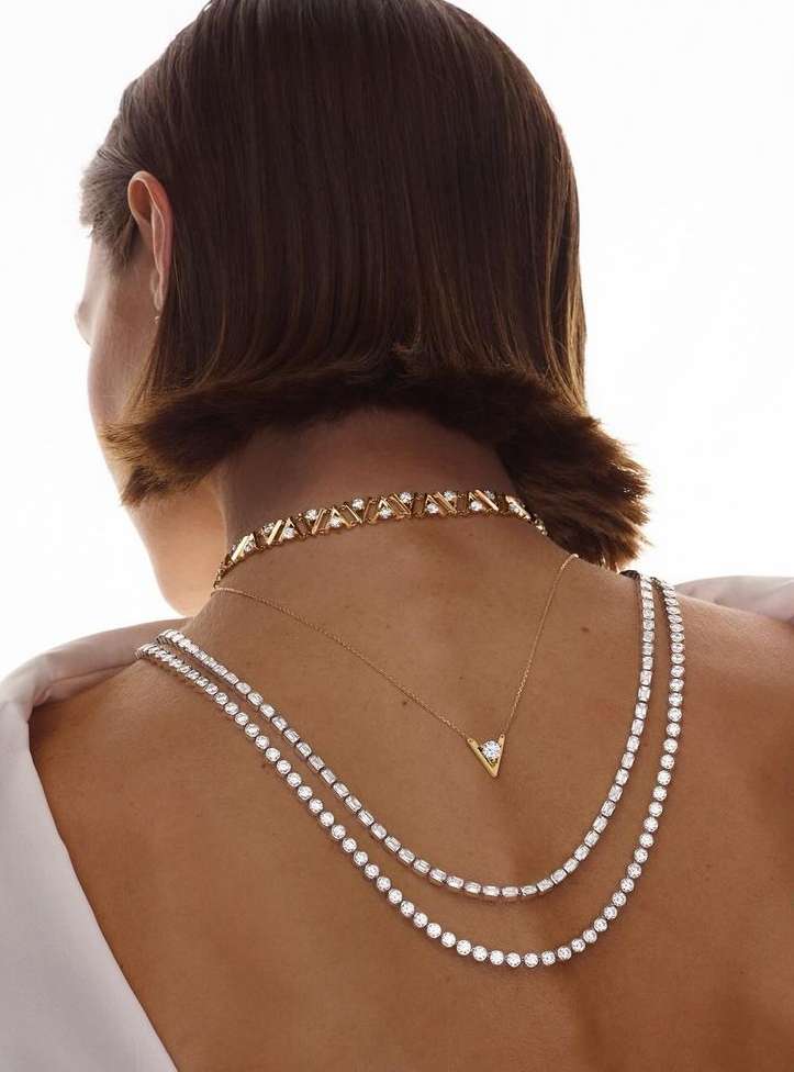 View of a woman's back and neck wearing gold and diamond necklaces in a studio with soft lighting and a white background.