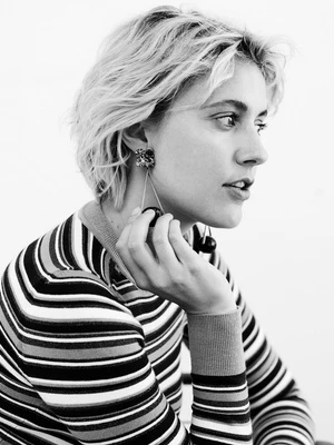 Black and white portrait of a woman with blonde hair in a striped shirt holding cherry earrings, set against a plain background.