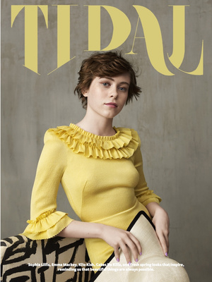 A portrait of actress Sophia Lillis wearing a yellow ruffled dress against a textured grey wall, photographed by Nadya Wasylko.