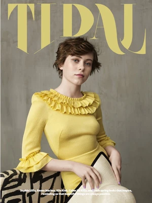 A portrait of actress Sophia Lillis wearing a yellow ruffled dress against a textured grey wall, photographed by Nadya Wasylko.