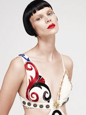 Model with blunt black bob and red lipstick wearing an embroidered white dress against white seamless backdrop