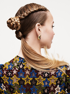 Profile of a woman with an elaborate braided hairstyle, wearing a star-patterned top against a plain white background.