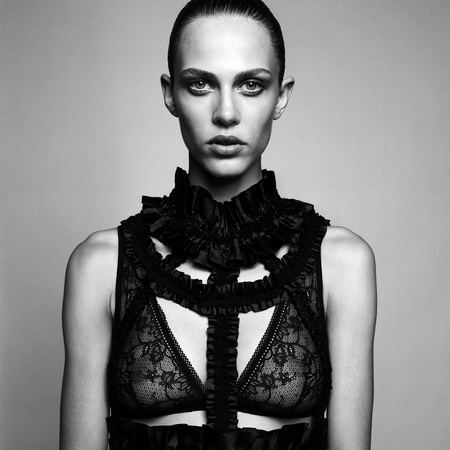 Striking black and white portrait of a woman with sleek hair, wearing a detailed black lace and ruffle top against a neutral backdrop.