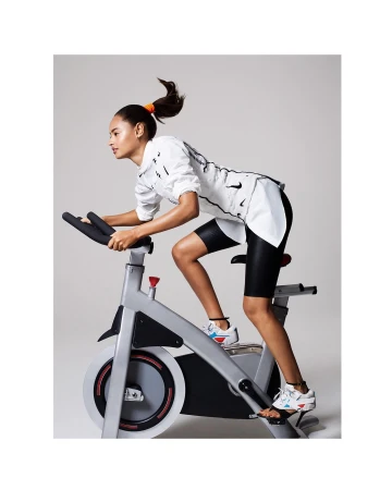 Athletic woman riding stationary exercise bike in fitness studio with modern workout gear and ponytail, wearing Nike athletic apparel.