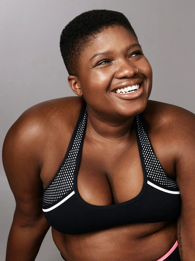 Smiling woman in athletic top looks up and to the side against a grey background in a fitness portrait with neutral colors.