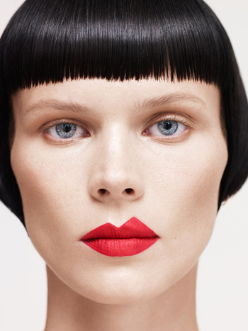 Close-up portrait of a model with short black blunt bob and vibrant red lipstick against a plain white background