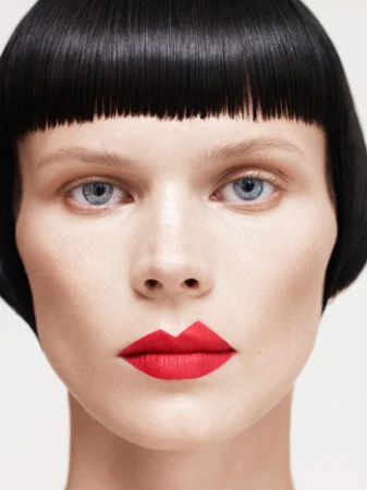 Close-up portrait of a model with short black blunt bob and vibrant red lipstick against a plain white background