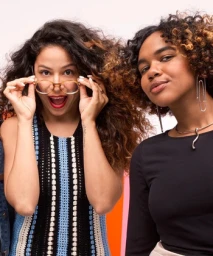 Two women with long curly hair posing indoors with bright color blocks in the background, photographed by Nadya Wasylko.