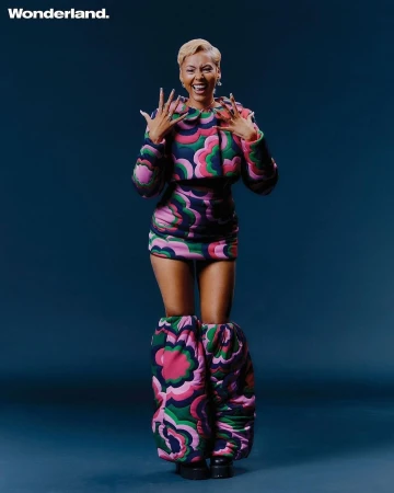 Woman with short blonde hair laughing in a matching floral patterned jacket, skirt, and oversized leg warmers.