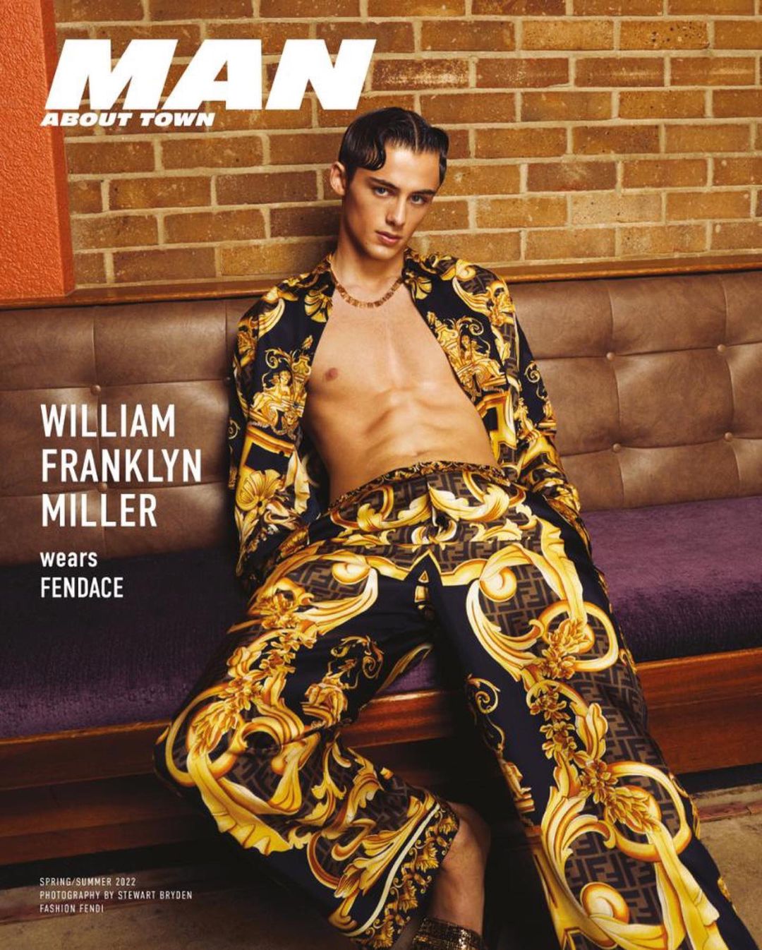Male model William Franklyn Miller poses in a patterned Fendace ensemble, seated on a purple sofa with a brick wall background for a magazine cover.