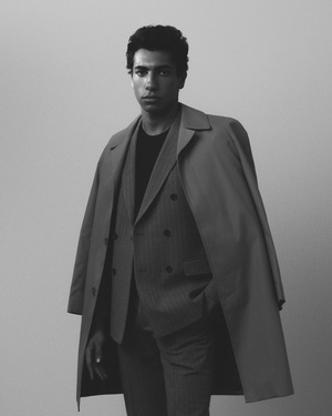 Portrait of a man in a double-breasted suit and long coat draped over his shoulders against a plain background