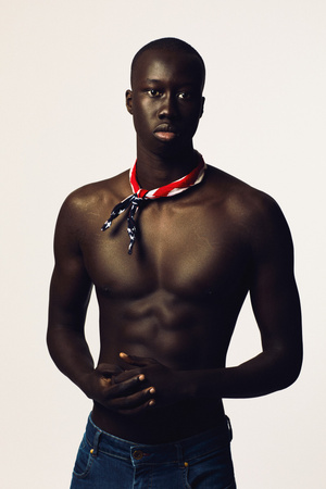 Portrait of a Black male model with a muscular build, wearing jeans and a patriotic bandana, in a light studio setting.