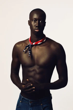 Portrait of a Black male model with a muscular build, wearing jeans and a patriotic bandana, in a light studio setting.