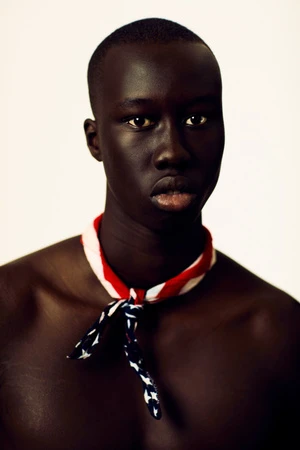 Portrait of an adult male with dark skin, looking directly at the camera, wearing a red, white, and blue bandanna around his neck.