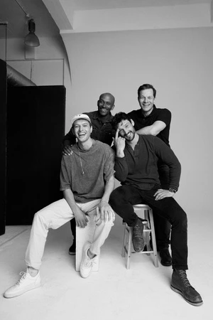 Group of four men smiling in a studio setting captured in black and white by photographer Stew Bryden.
