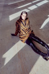 Woman in tiger stripe sweater and tall black boots seated on a wooden floor under directional light