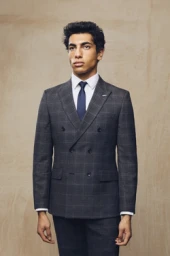 Man wearing a charcoal plaid double breasted suit with a white shirt and blue tie against a textured backdrop