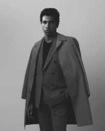 Portrait of a man in a double-breasted suit and long coat draped over his shoulders against a plain background