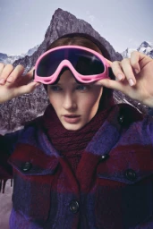 Woman wearing pink ski goggles and a purple plaid coat against a mountain backdrop photographed by Stew Bryden