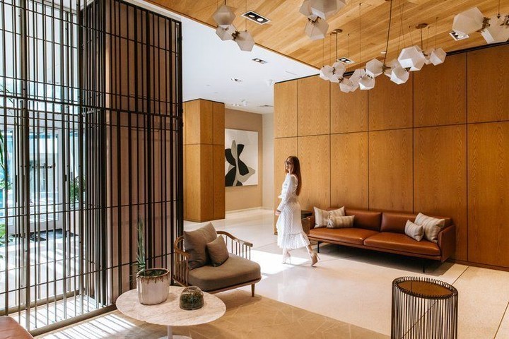 Woman in white dress walks through a modern interior space with wood paneling, contemporary furniture, and decorative geometric lighting.
