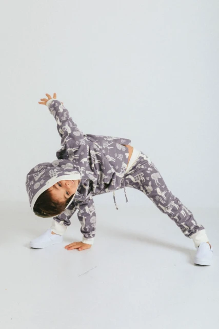 Child in a patterned hoodie and pants strikes a playful pose with one hand on the floor in a bright studio, showcasing active kids' fashion.