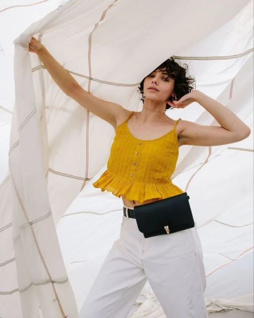 Woman wearing a yellow top and white jeans poses in front of a grid-patterned cloth, creating a fashion-forward, light and airy visual.