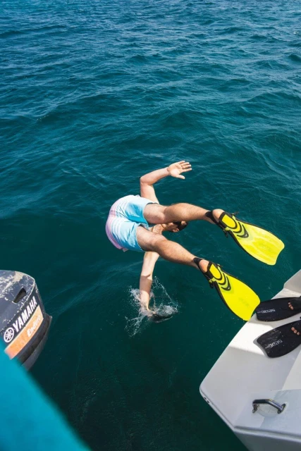 Adult dives headfirst into turquoise water from a boat wearing fins; splashes visible. Yamaha engine and hull visible.
