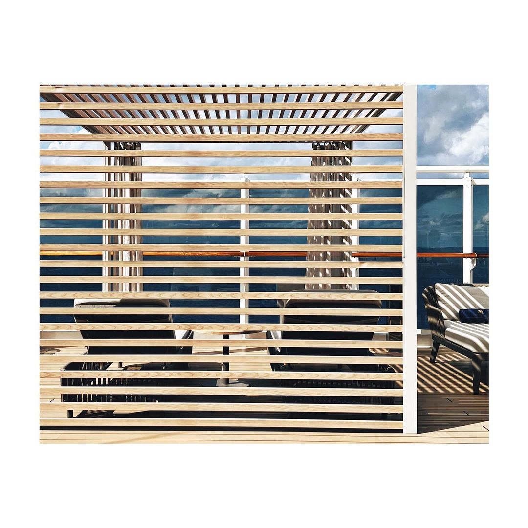 Exterior of a luxury cruise ship deck featuring a partially shaded lounge area with modern furniture and views of the ocean and sky.