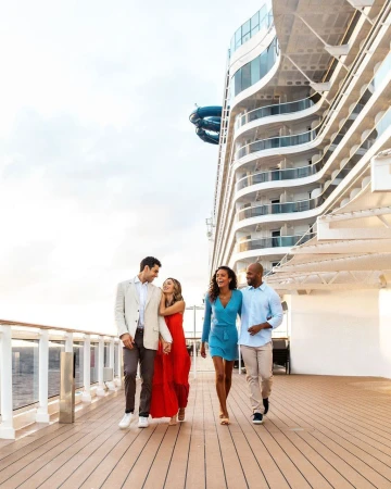 Two couples walking along a cruise ship deck, enjoying ocean travel together in formal attire under an overcast sky.