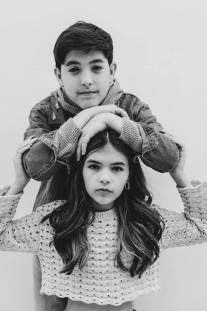 Portrait of a young boy resting his arms on the head of a girl wearing a textured knit sweater against a plain white background