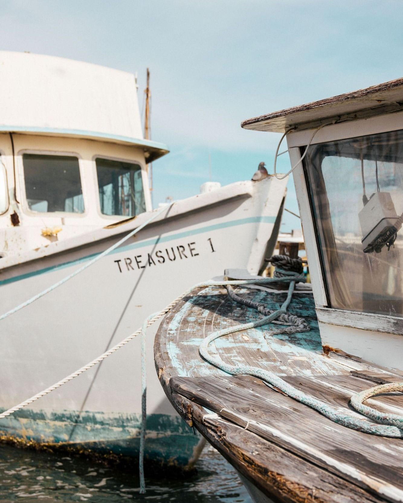 Two docked vintage fishing boats, one labeled 'Treasure 1,' are captured in a close-up shot with cloudy skies in the background.
